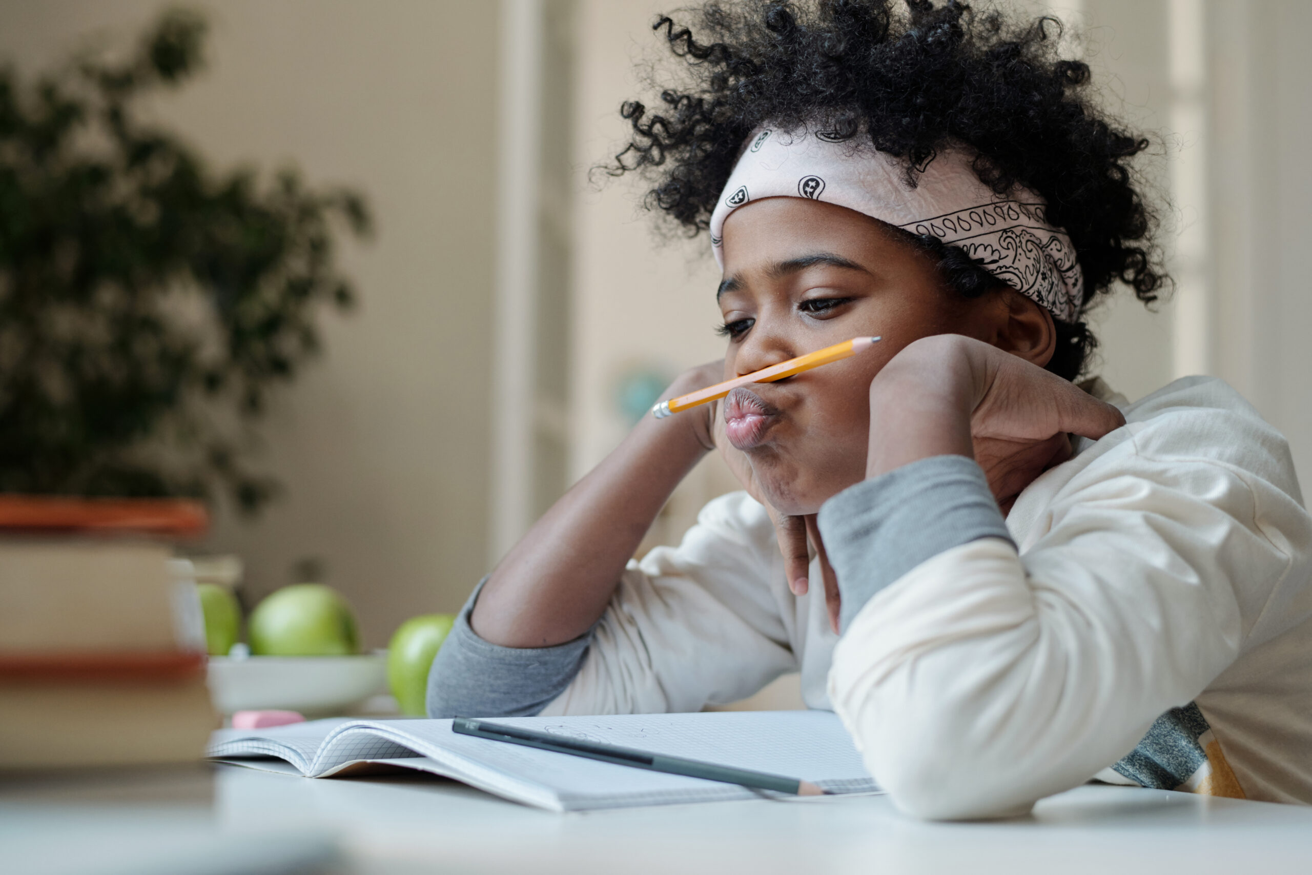 Distracted and lazy schoolboy reluctant to do homework sitting by desk